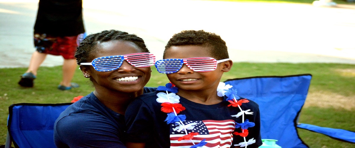 Two children wearing US Flag sunglasses and red, white and blue leis and a sweater with the American flag.