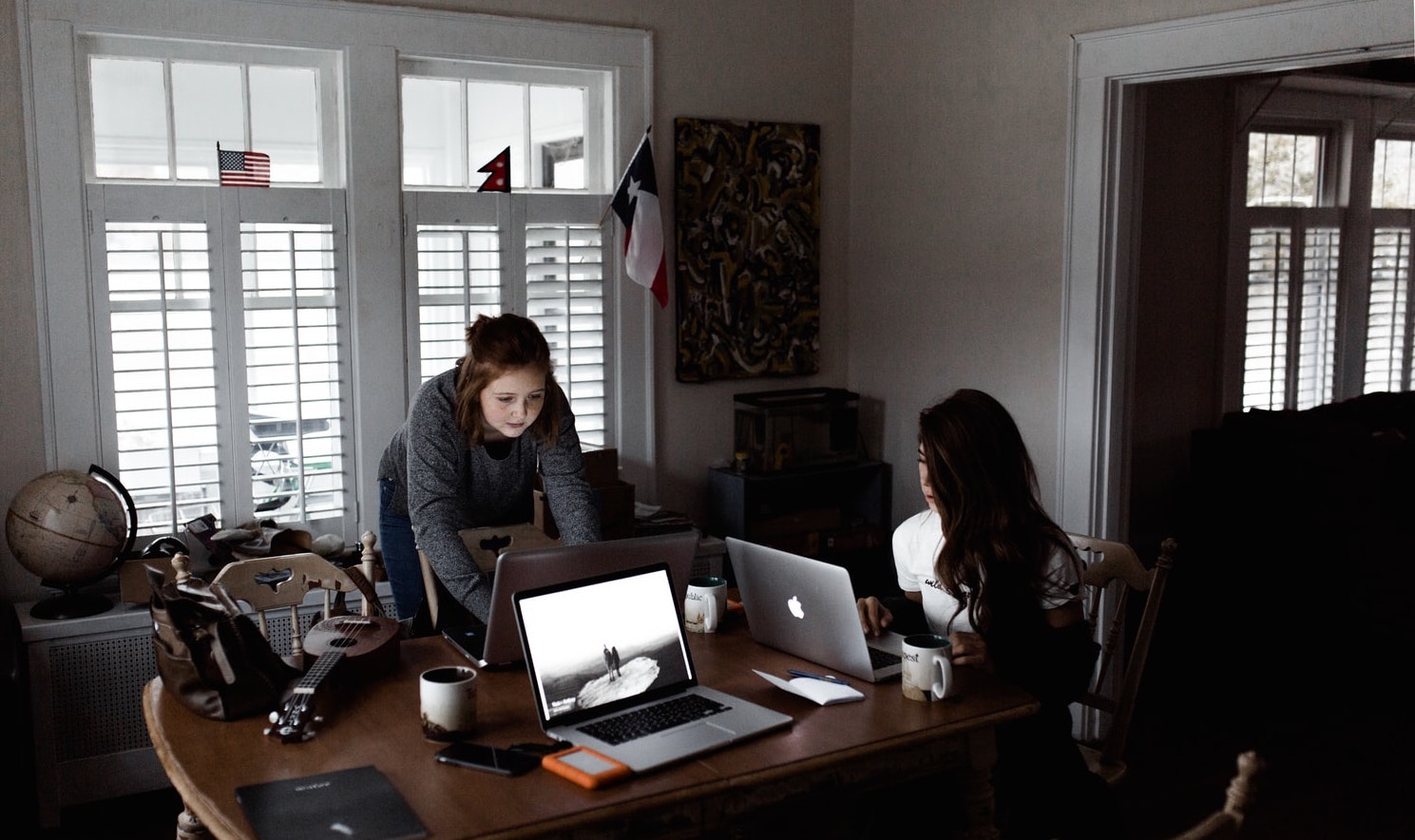 A photo of co-workers seated and standing around a table while using their laptop computers.