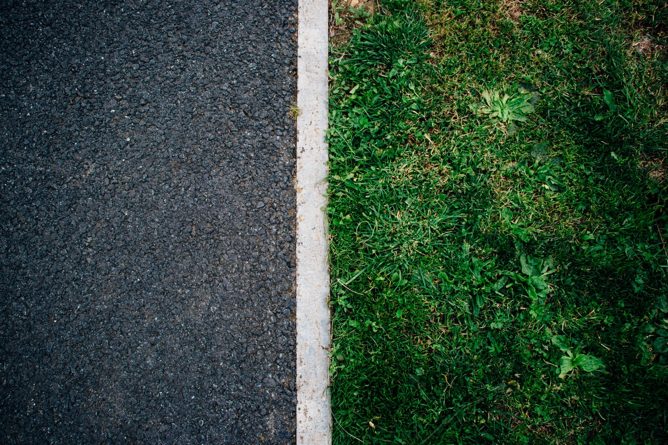 A photo of two contrasting images. One on left is a black roadway and the one on the right is a patch of green grass.