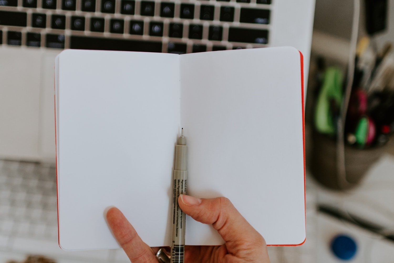 A photo of a person in front of a laptop computer holding an open notepad and a pen.