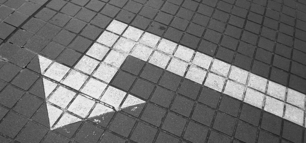 A photo of a square tiled sidewalk with a white arrow pointing straight and then left.