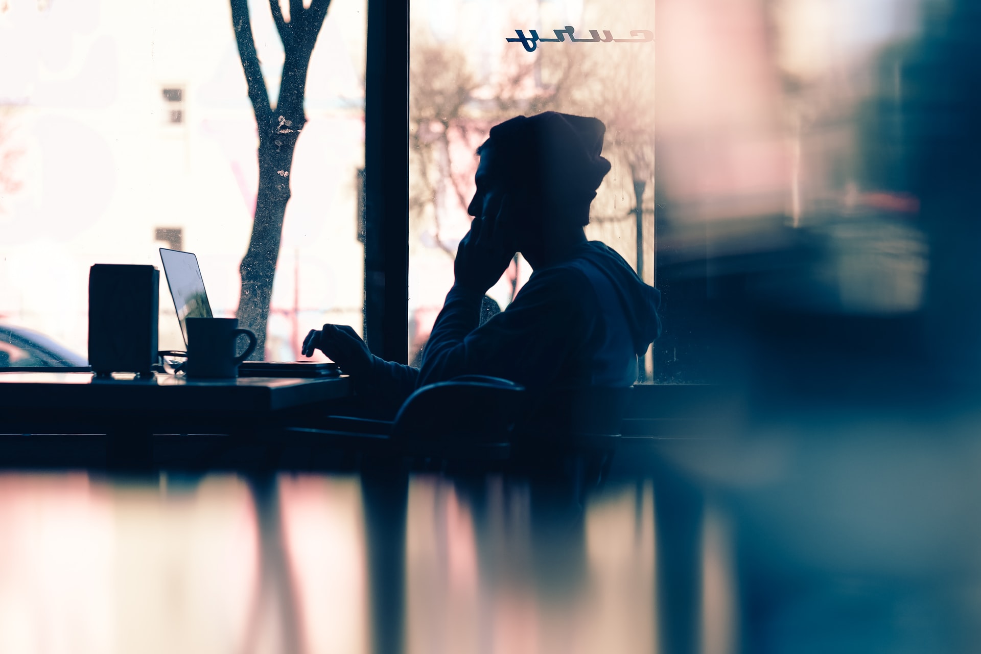 Image of a man seated at a coffee shop typing on a laptop PC.